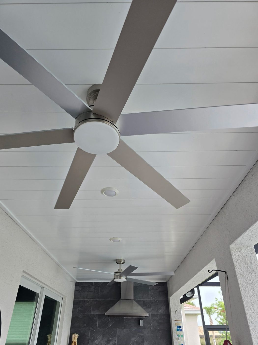 White shiplap lanai ceiling with oversized fans above an outdoor kitchen